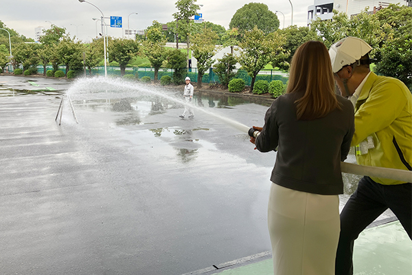 防火訓練の様子、女性と男性がホースで放水している画像